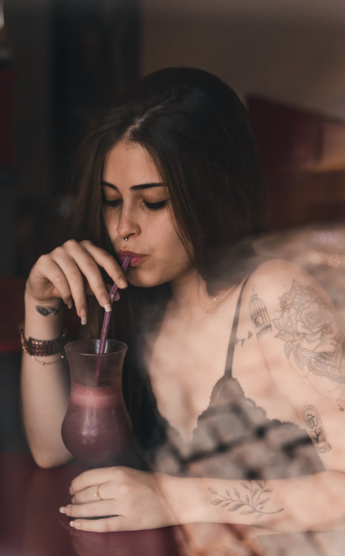 Stylish woman with tattoos sipping a drink through a straw indoors in Brazil.